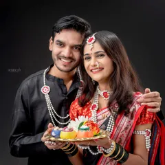 A happy couple poses for a classic portrait during their Makarsankranti shoot. The woman holds a traditional thali, and both are adorned with festive *halwyache dagine*.