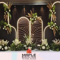 This modern stage design uses clean lines and dramatic lighting to create a sophisticated ambiance. The illuminated white arches contrast beautifully with the dark backdrop, while arrangements of white flowers and pampas grass add softness and texture.