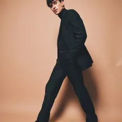 A full-length shot of a pinstripe suit against a neutral background. The styling is clean and sharp, focusing on the modern silhouette and the model's confident stride to create a powerful image of contemporary tailoring.