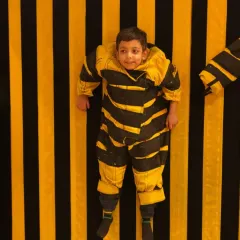 Getting stuck is half the fun on our velcro wall! A child dressed in a bee-themed suit hangs on the wall, a perfect photo moment.