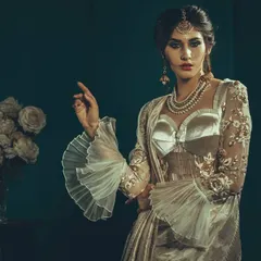 An editorial shot featuring a modern take on the saree with dramatic ruffled sleeves. The vintage color grading and soft lighting give the image a timeless, painterly quality.