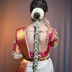 A stunning bridal plait decorated with pearl and green stone studded jewellery pieces along its length. The look is completed with a traditional jasmine gajra around the base.