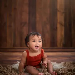 A look of pure wonder. Against a dark wood background, this baby's expressive face tells a beautiful story all on its own. This is the power of minimalist baby photography.