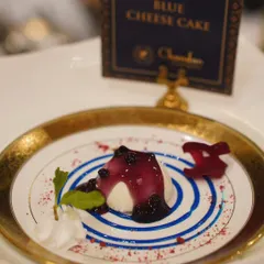 An artfully plated Blue Cheese Cake, topped with a blueberry compote and served on a plate with a decorative blue swirl. A sophisticated and savory-sweet dessert.