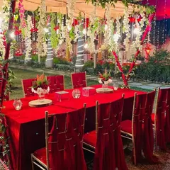 A royal red-themed seating arrangement for guests. The long table is covered in red velvet, with matching chair drapes and a canopy of hanging flowers above.