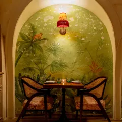 An intimate two-seater nook at Los Cavos, framed by a hand-painted tropical mural within a textured archway. This design choice creates cozy pockets within the larger space, perfect for quiet conversations.