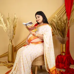 A peaceful moment of reflection. This mom-to-be, dressed in a classic white and red border saree, reads a spiritual book, adding a layer of personal meaning to her maternity session.