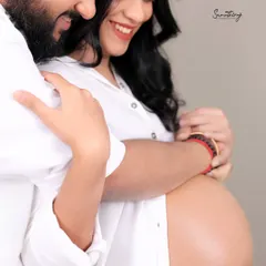 A close-up of a couple's embrace, focusing on the baby bump. The simple white shirts and their happy smiles create a pure and joyful image of their connection.