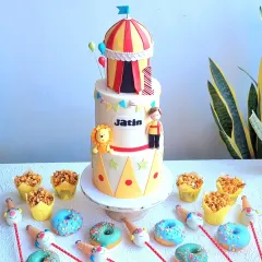 A full carnival-themed dessert table, including a three-tiered cake, caramel popcorn cups, themed donuts, and clown cakepops.