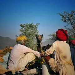Two traders in traditional Rajasthani attire sit with their camel, which curiously peeks between them, at the Pushkar Fair.