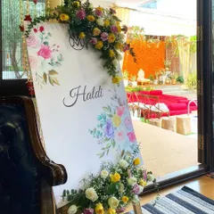 A pretty welcome sign for a Haldi ceremony, adorned with fresh yellow roses and baby's breath. In the background, you can see the main event space with its bright marigold decor, setting the tone for a fun-filled event.