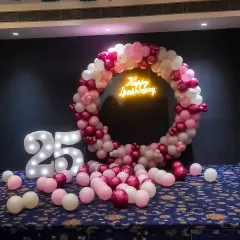 A beautiful setup to celebrate a 25th anniversary. The large balloon ring in pink and white, paired with a neon sign and light-up numbers, creates a perfect backdrop for capturing memories of this special milestone.