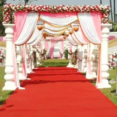 A classic wedding entrance gate with white pillars, draped in pink and white fabric, leading to a red carpet aisle for a grand welcome.