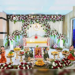 An elaborate stage for an engagement or baby shower, featuring a stunning floral arch of red and white roses, a comfortable diwan, and a full display of traditional gifts and fruits.