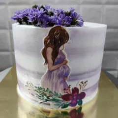 A beautiful baby shower cake for a mom-to-be. The design features a watercolor effect and is topped with fresh purple flowers.