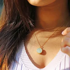 A delicate, sunlit shot of a model wearing a simple, round gemstone necklace. The natural lighting enhances the beauty of the piece and creates a soft, feminine mood.