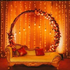 A classic and romantic stage for a ring ceremony or reception. The circular arch is decorated with flowers and paired with a vintage-style sofa against a backdrop of warm fairy lights.