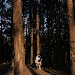 A wide shot showing the scale and majesty of the forest. The couple, small in the frame, is enveloped by the towering trees, creating a sense of quiet intimacy in a vast landscape.