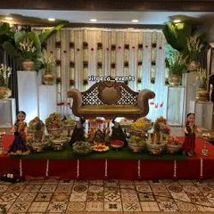 Here is a full view of a traditional Seemantha decoration. The stage is set with a backdrop of jasmine flower strings, banana leaves, and a beautiful arrangement of seer plates with dolls and peacock figures.