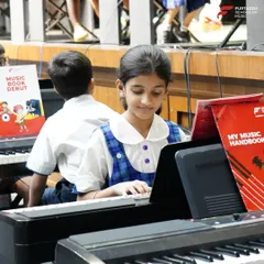 A close-up of a young student focused on her keyboard during a school recital. With our "My Music Handbook" and dedicated practice, students follow a structured curriculum that builds their skills progressively.