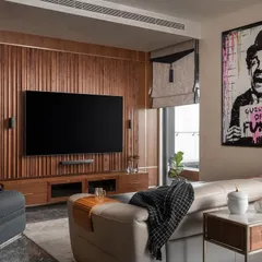 The media room from our "Quintessence" project, designed for entertainment and relaxation. The custom wood-paneled wall integrates the television and sound system, while playful art adds a touch of fun to the sophisticated space.