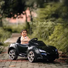 Tiny treasures and moments of childhood delight. A happy toddler enjoys a ride in her convertible toy car on a path in the park.
