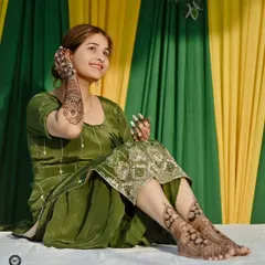 A happy bride posing with her full bridal mehndi, including detailed designs on her feet.