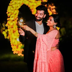 A magical night-time shot of a couple holding sparklers in front of a heart-shaped arch of lights, perfect for a festive pre-wedding theme.
