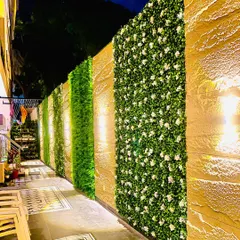 A full view of a long compound wall featuring alternating panels of stone, dense green foliage, and white flowering plants. This design breaks up the monotony of a long wall and adds significant curb appeal.