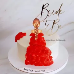 A pretty cake for a bride-to-be. This elegant design features a topper of a bride in a beautiful red dress, celebrating her upcoming wedding.