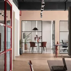 This view captures the open and connected feel of the studio. The herringbone floor separates common areas from work sections, while glass partitions maintain visual flow. The red-framed pantry door adds a bold pop of color.
