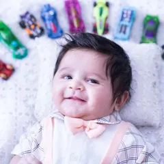 This three-month-old cutie is ready to race. Lying on his back, he is surrounded by an arc of colorful Hot Wheels cars.