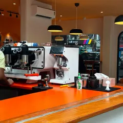 The heart of the cafe: the espresso station. The bright orange countertop makes a bold statement, reflecting the brand's energy, while the professional equipment is laid out for optimal workflow for the baristas.