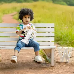 A toddler boy with amazing curly hair sits on a bench during his outdoor second birthday shoot.