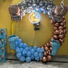 A stylish baby shower backdrop using a mix of metallic bronze and classic blue balloons. The 'Oh Baby' neon sign in the center of the circular arch adds a trendy, modern feel.