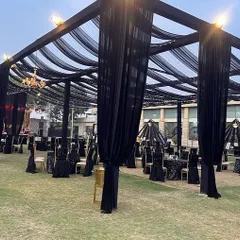 This outdoor evening setup features a large black canopy with elegant draping and chandeliers. The sophisticated black theme provides a chic and modern setting for a corporate cocktail event or dinner.