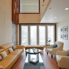The first-floor living room of the Gupta Residence is a modern, inviting space with contemporary seating and wooden flooring. Large windows fill the room with natural light, while backlit shelving and framed photographs add personal character.