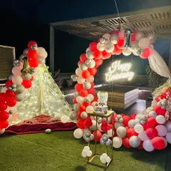 This cozy and stylish terrace setup is perfect for a first anniversary. It features a beautiful red, white, and silver balloon arch, a lit-up teepee for a romantic seating area, and a custom neon sign to celebrate your special day.