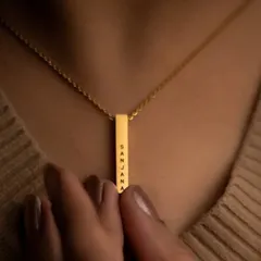 This close-up shows a gold bar pendant engraved with the name 'Sanjana'. The clean font and minimalist design make it a versatile piece, perfect for wearing alone or layering with other necklaces.