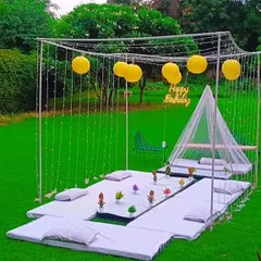 A picnic-style party setup on a lush green lawn. This arrangement includes low seating with cushions and a small canopy, perfect for a relaxed daytime celebration.
