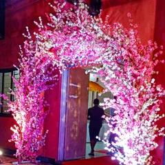 A modern entrance arch made with artificial pink cherry blossom branches. The arch is internally lit, creating a beautiful and bright floral gateway for an evening event.