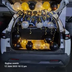 A car boot or dickey decoration is a great way to surprise someone. This setup includes a 'Happy Birthday' banner, fairy lights, and balloons in black, gold, and silver, creating a perfect movie-style surprise moment.
