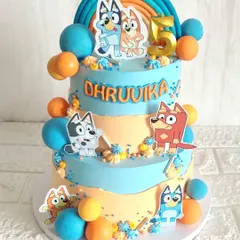 A fun and colorful two-tier cake for a fifth birthday, celebrating the popular show Bluey and Bingo. The design is decorated with edible character toppers and bright, playful chocolate spheres.