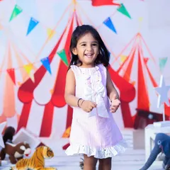 A happy two-year-old girl enjoying her carnival-themed birthday shoot. Her bright smile and the colorful circus tent backdrop create a festive atmosphere.