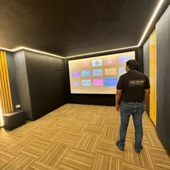 The project is nearing completion. Our technician inspects the finished room, which features beautiful wood-paneled acoustic walls and patterned flooring, ensuring every element of the home theater design is executed to perfection before final calibration.
