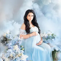 A beautiful, fantasy-themed portrait of a mother-to-be. She is seated in a light blue gown amidst a bed of blue flowers and soft, cloud-like textures, creating a serene and magical atmosphere.