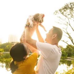 A couple joyfully lifts their small dog into the air against a sun-flared sky, a beautiful silhouette of family love.
