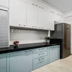 A sleek L-shaped kitchen with light blue base cabinets and white overheads. The design seamlessly integrates the refrigerator and uses a subway tile backsplash for a clean, modern finish.