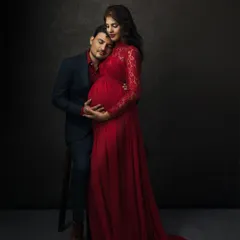 A husband rests his head gently on his wife's baby bump. This intimate fine art portrait, with its rich red gown and dark background, feels like a classic painting.