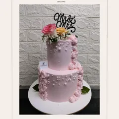A beautiful two-tiered pink anniversary cake to celebrate a special couple. Featuring a "Mr & Mrs" topper, fresh flowers, and elegant piping details, it’s a sweet way to honor a lasting love story.